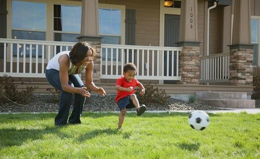 A mom and her son playing soccer in the front yard